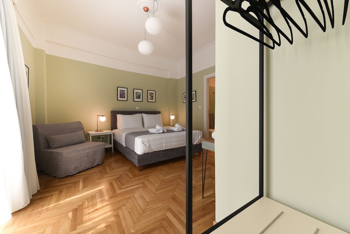 Een moderne slaapkamer met een bed, een grijze bank en een nachtkastje met een lamp.