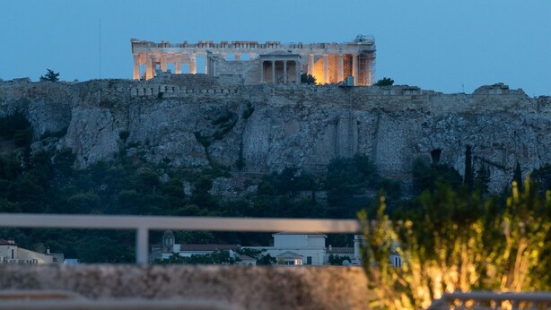 A view of ancient ruins on a cliff with a modern building in the background. - Athens Stories (Athens)