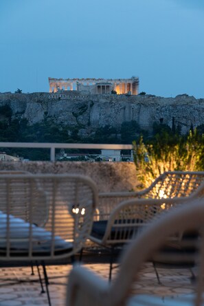 A view of ancient ruins on a cliff with a modern building in the background. - Athens Stories (Athens)