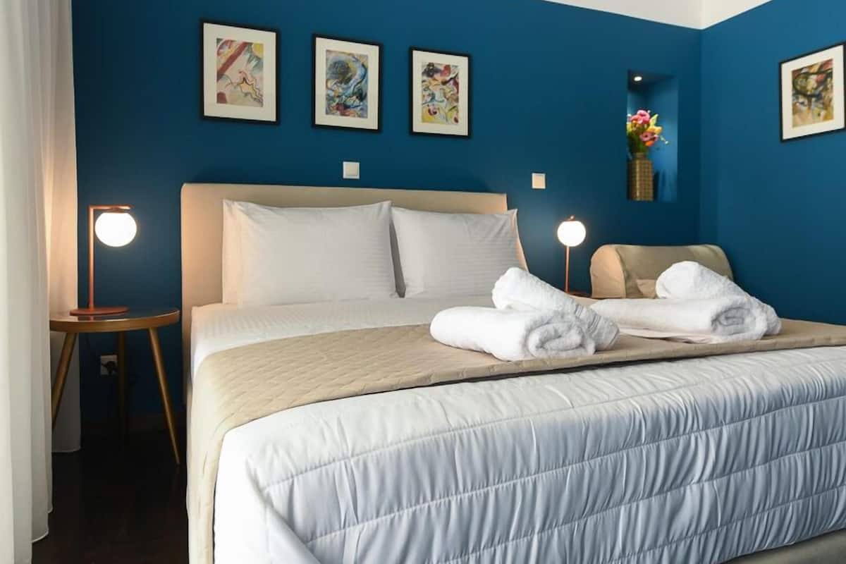 A hotel room with a bed, white linens, a blue accent wall, and framed artwork.