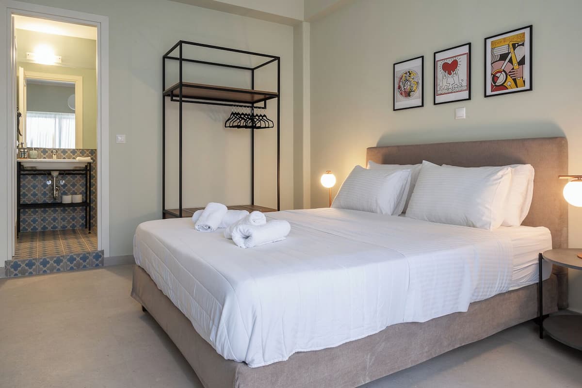 A hotel room with a bed, a nightstand, a wall-mounted shelf, and a bathroom visible through an open door.