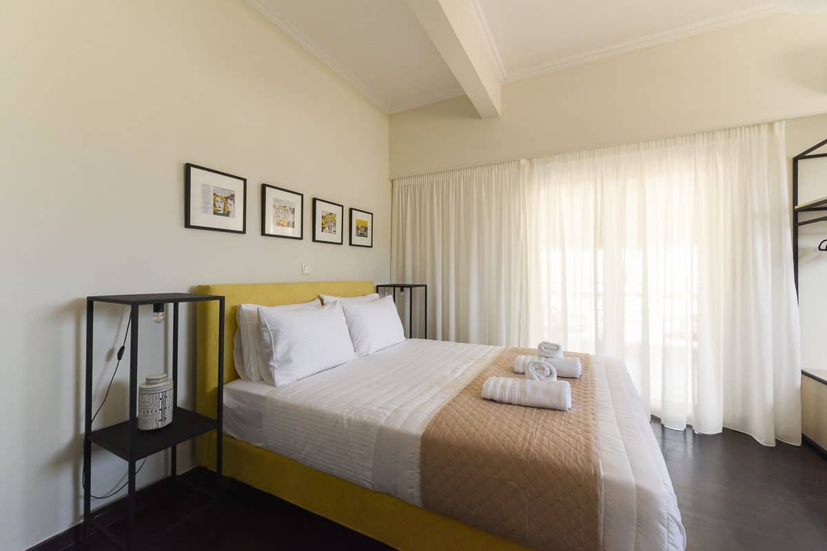 A neatly made bed with white linens, a yellow headboard, and a bedside table with a lamp and a decorative item.