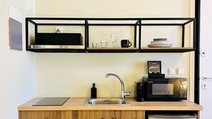 A compact kitchen with wooden cabinets, a stainless steel refrigerator, a built-in microwave, and a sink with a faucet. - Athens Stories (Athens)