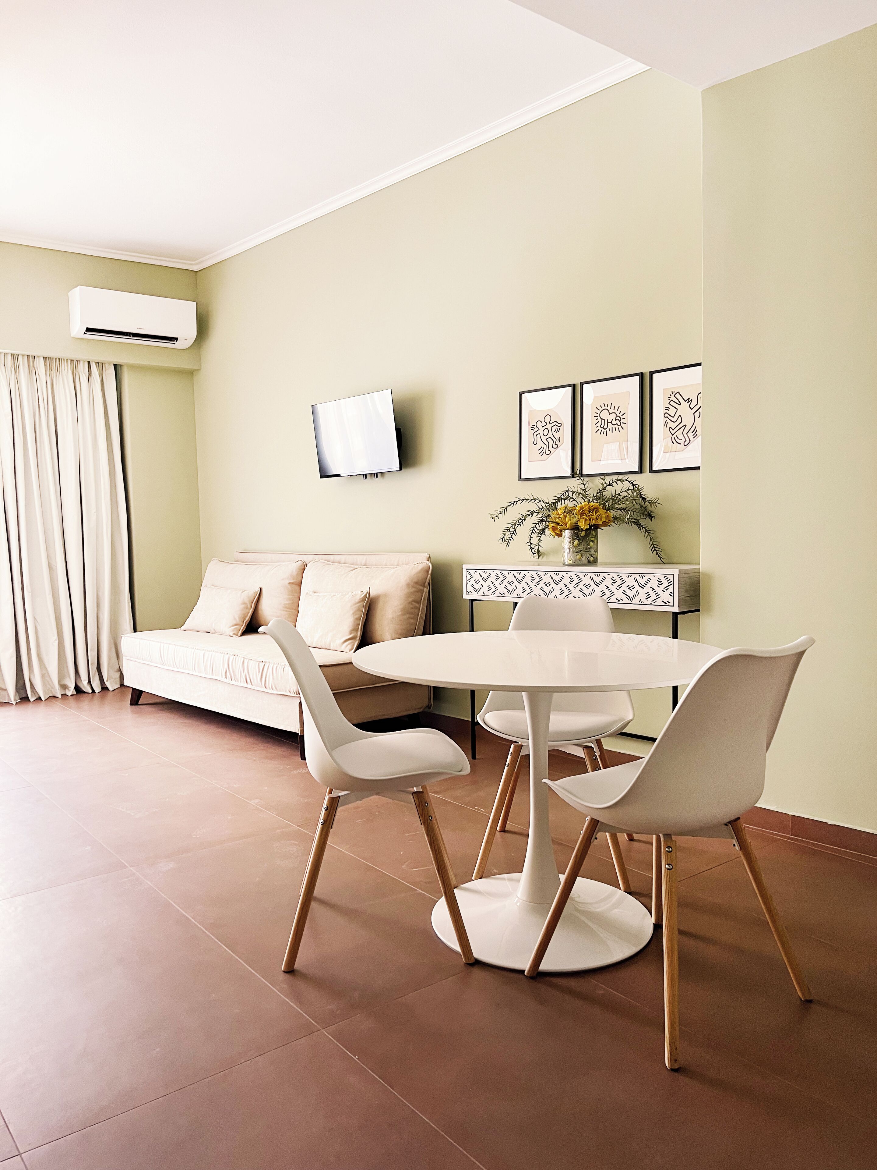 A modern living room with a sofa, a dining table with chairs, a flat-screen TV, and framed artwork on the wall.