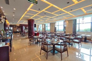 A spacious restaurant with multiple dining tables and chairs, a bar area, and large windows allowing natural light.
