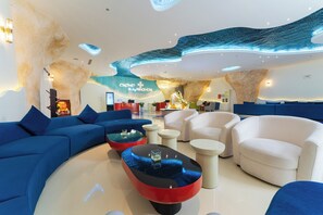 Un hall d’hôtel moderne avec un canapé bleu incurvé, des fauteuils blancs et une table basse rouge.