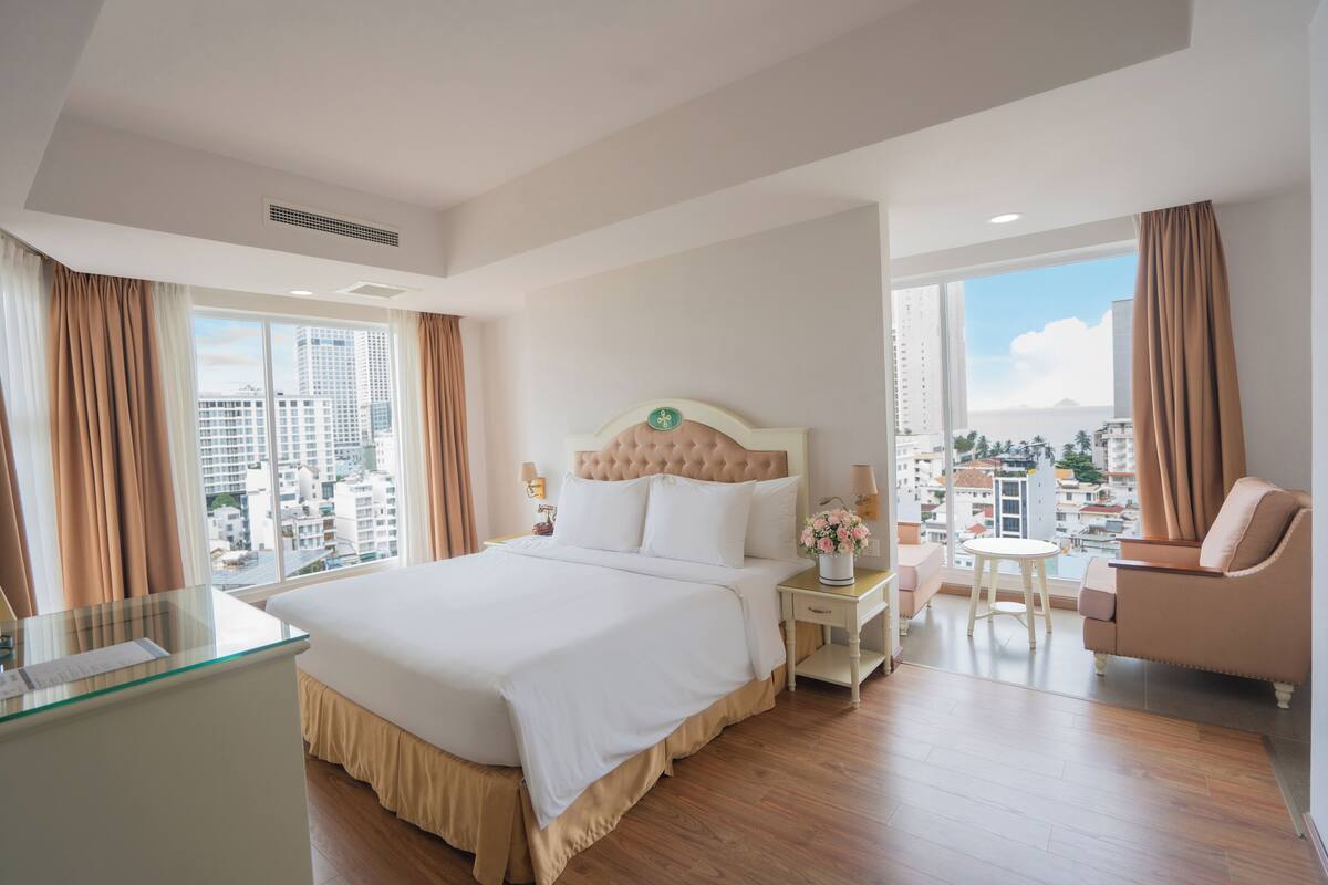 Hotelkamer met een groot bed, een glazen bureau, een stoel en uitzicht op de stad.