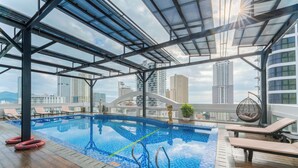 An indoor swimming pool with a view of city buildings, lounge chairs, and a hanging chair. - Nha VIET Nha Trang Hotel (Nha Trang)
