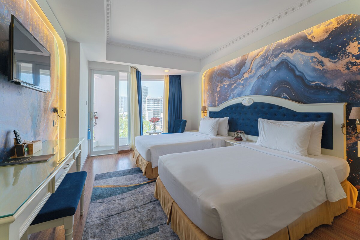 Ein Hotelzimmer mit zwei Betten, einem Schreibtisch, einem Fernseher und einem großen, abstrakten Wandbild.
