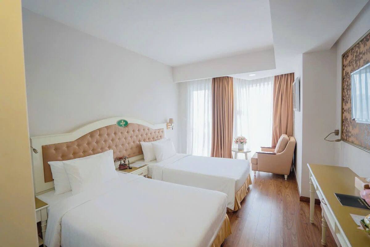 Een hotelkamer met twee bedden, een bureau, een stoel en een raam met gordijnen.