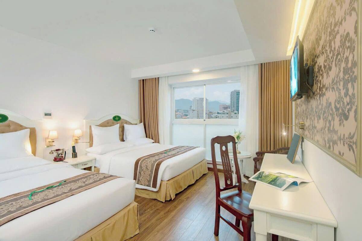 Hotelkamer met twee bedden, een bureau, een stoel, een aan de muur bevestigde televisie en uitzicht op de stad.