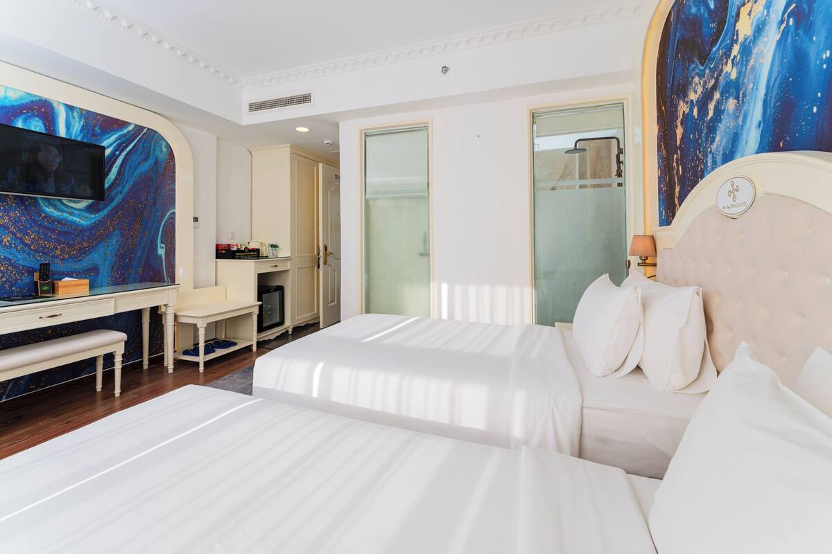 Een hotelkamer met twee bedden, een bureau, een televisie en een groot schilderij aan de muur.