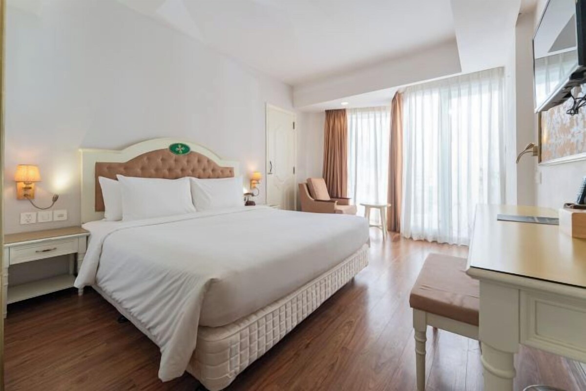 A hotel room with a large bed, bedside tables, a desk, and a chair.