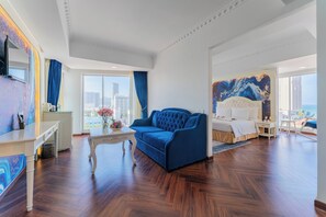 Ein geräumiges Hotelzimmer mit einem großen Bett, einem blauen Sofa, einem weißen Couchtisch und Blick auf die Stadt.