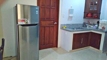 Una cocina compacta con un refrigerador de acero inoxidable, una puerta de madera, un lavamanos empotrado y una pequeña encimera con un hervidor.