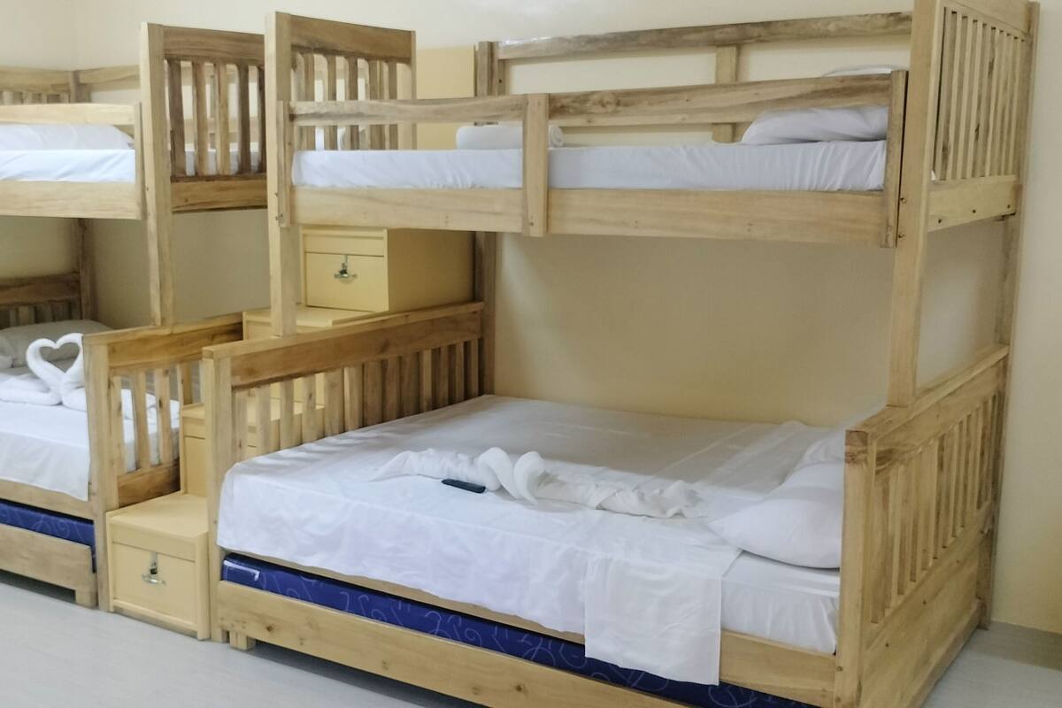 Una habitación con cuatro literas ubicadas en un rincón, cada una con una mesita de noche y un cajón.