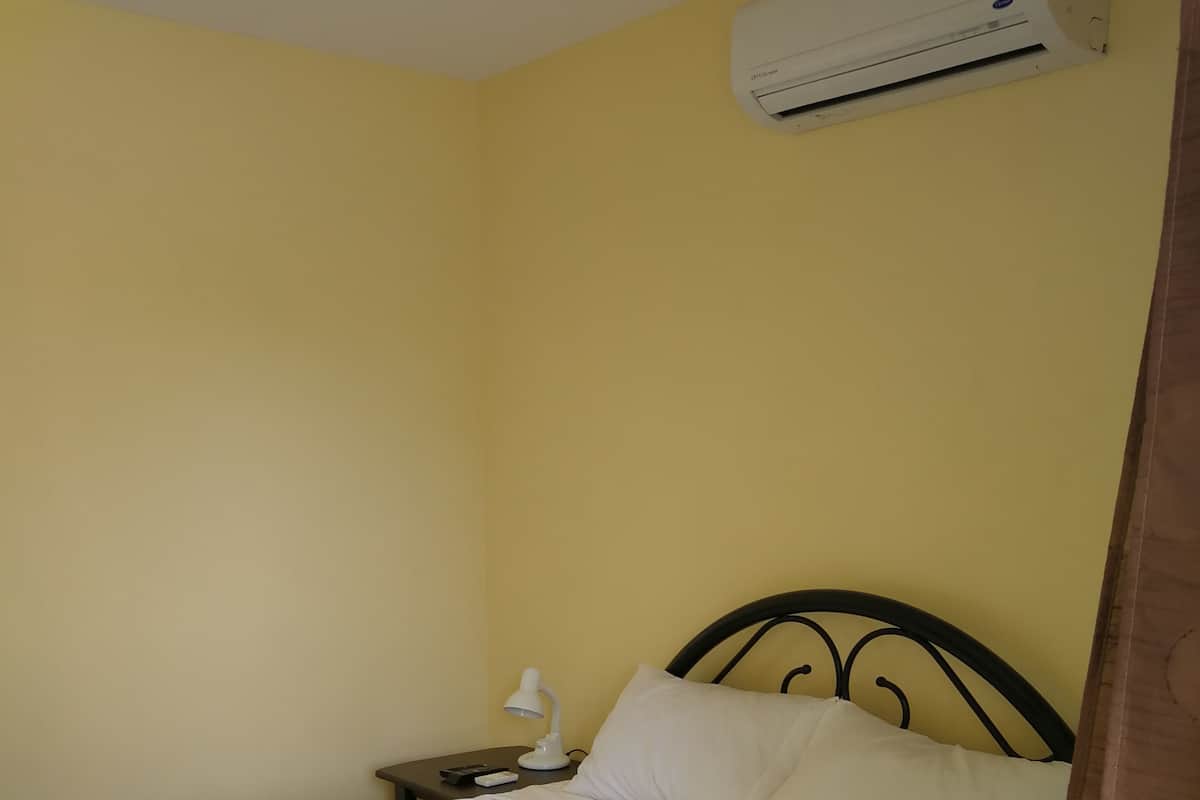 Una cama en una habitación con pared amarilla y un equipo de aire acondicionado encima.