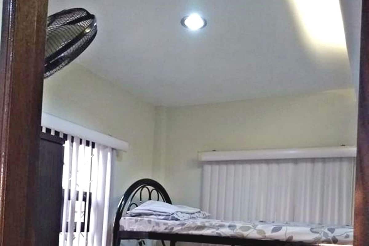 Una habitación pequeña con una cama individual y literas, un radiador y una ventana con persianas.
