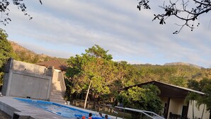 A swimming pool area with steps leading into the water, surrounded by trees and a hillside in the background. - Hidaway Resort (San Antonio)