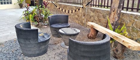 Outdoor seating with wicker chairs and a round table, surrounded by gravel and plants.