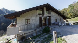 A rustic mountain lodge with a stone facade, wooden balcony, and outdoor seating area. - Agriturismo Cascina Cornella (Cremeno)