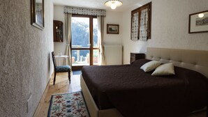 A bedroom with a large bed, a chair, a window with curtains, and a radiator. - Agriturismo Cascina Cornella (Cremeno)