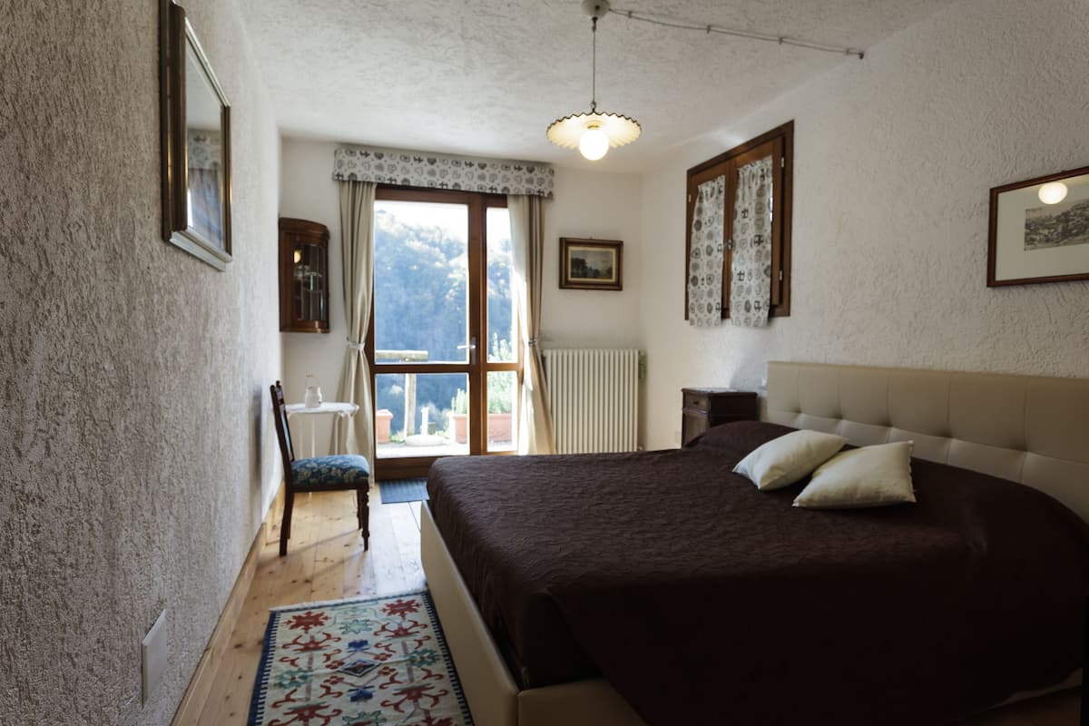 Een slaapkamer met een groot bed, een stoel, een raam met gordijnen en een radiator.