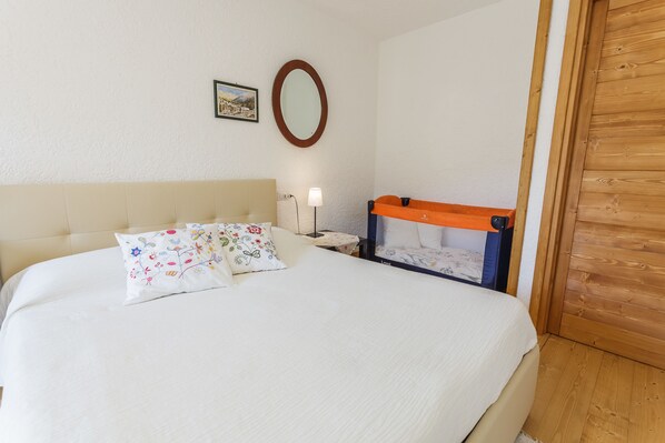 Una cama bien hecha con un cojín floral, una mesita de noche con lámpara y un armario de madera.