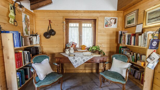 A cozy room with wooden walls, a wooden table, two chairs, and bookshelves filled with books. - Agriturismo Cascina Cornella (Cremeno)