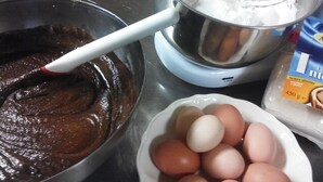 A kitchen with a mixing bowl containing a dark mixture, a bowl of eggs, and a container of flour. - Agriturismo Cascina Cornella (Cremeno)
