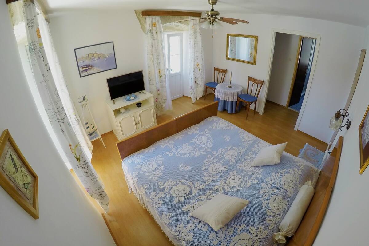 Quarto com cama grande, televisão, escrivaninha com cadeiras, ventilador de teto e espelho.