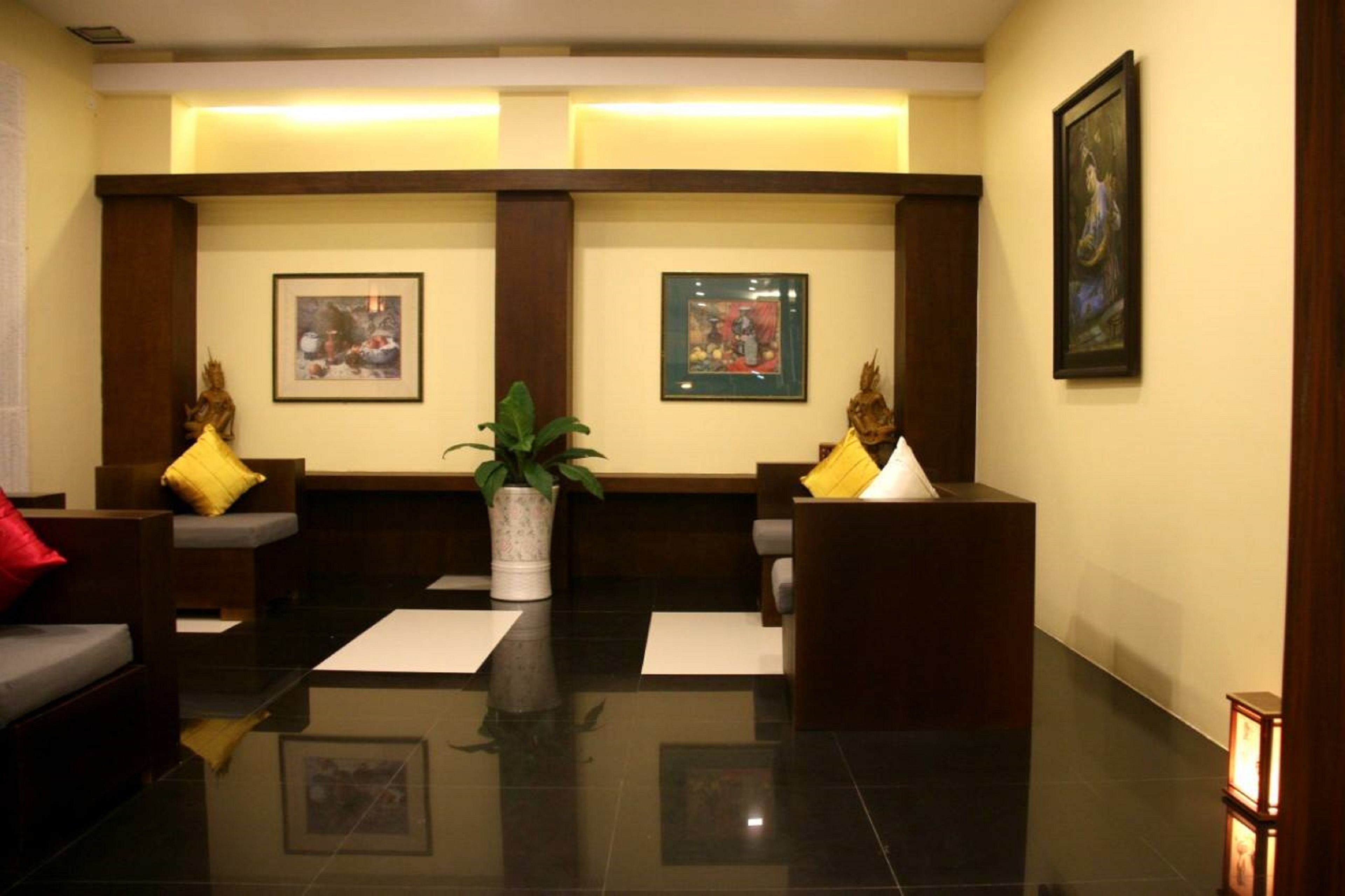 A lobby with a reception desk, two sofas with yellow cushions, a potted plant, and framed artwork on the walls.
