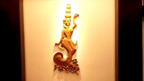 A wall-mounted sculpture of a figure with a tail, placed above a sofa with cushions. - Golden Guest Hotel Dawei (Dawei)