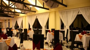 A restaurant with multiple tables set for dining, white curtains, and a high ceiling with exposed beams. - Golden Guest Hotel Dawei (Dawei)