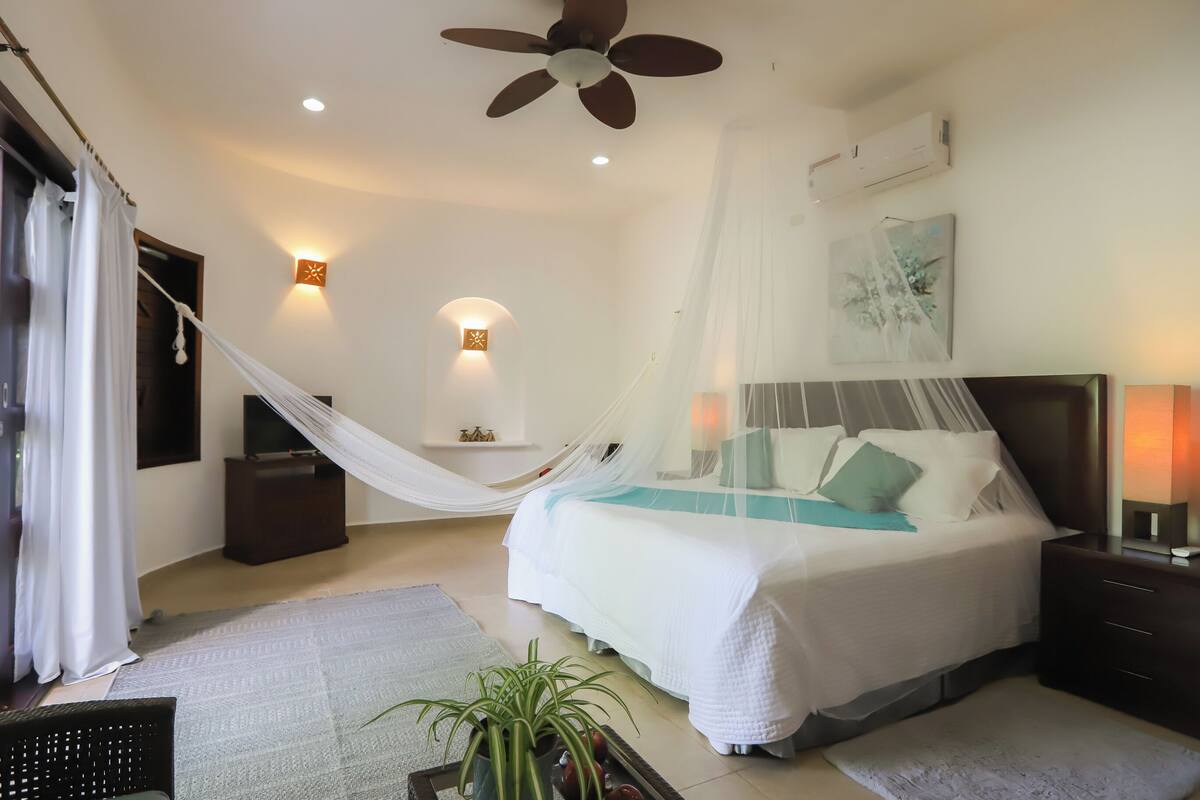 Ein Schlafzimmer mit Bett, Nachttisch, Wandklimaanlage, Deckenventilator und einer Hängematte.
