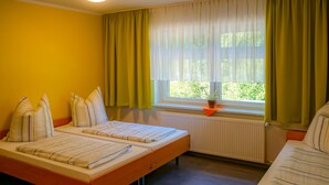 Een kamer met twee bedden, een raam met gordijnen, een radiator en een plant in een pot op de vensterbank.