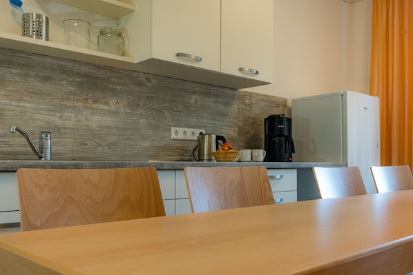 A modern kitchen with wooden cabinets, a stainless steel sink, and a dining area with a wooden table and chairs.