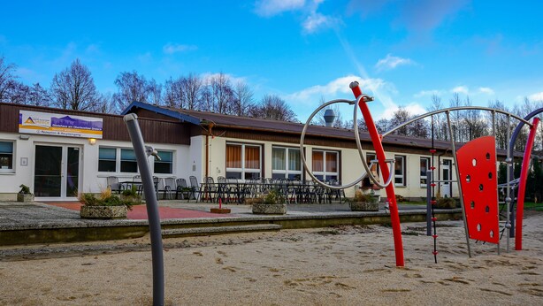 Een gebouw met een bord dat een receptie en eetruimte, terras en een speeltuin met rode apparatuur aangeeft.