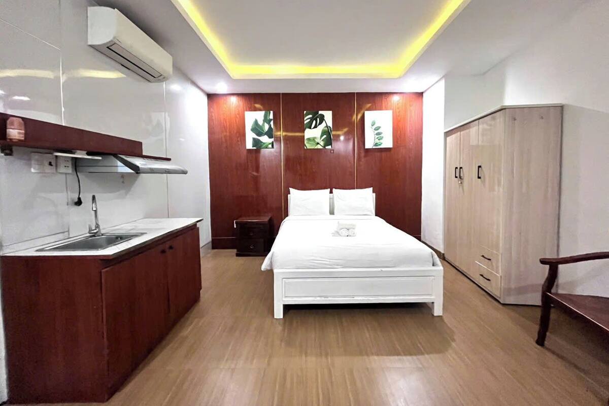 A bedroom with a bed, bedside table, wardrobe, and a kitchenette area with a sink and countertop.