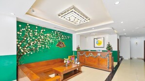 A reception area with a green wall, wooden bench, reception desk, and a framed picture on the wall. - The Samson Boutique Hotel (Da Nang)