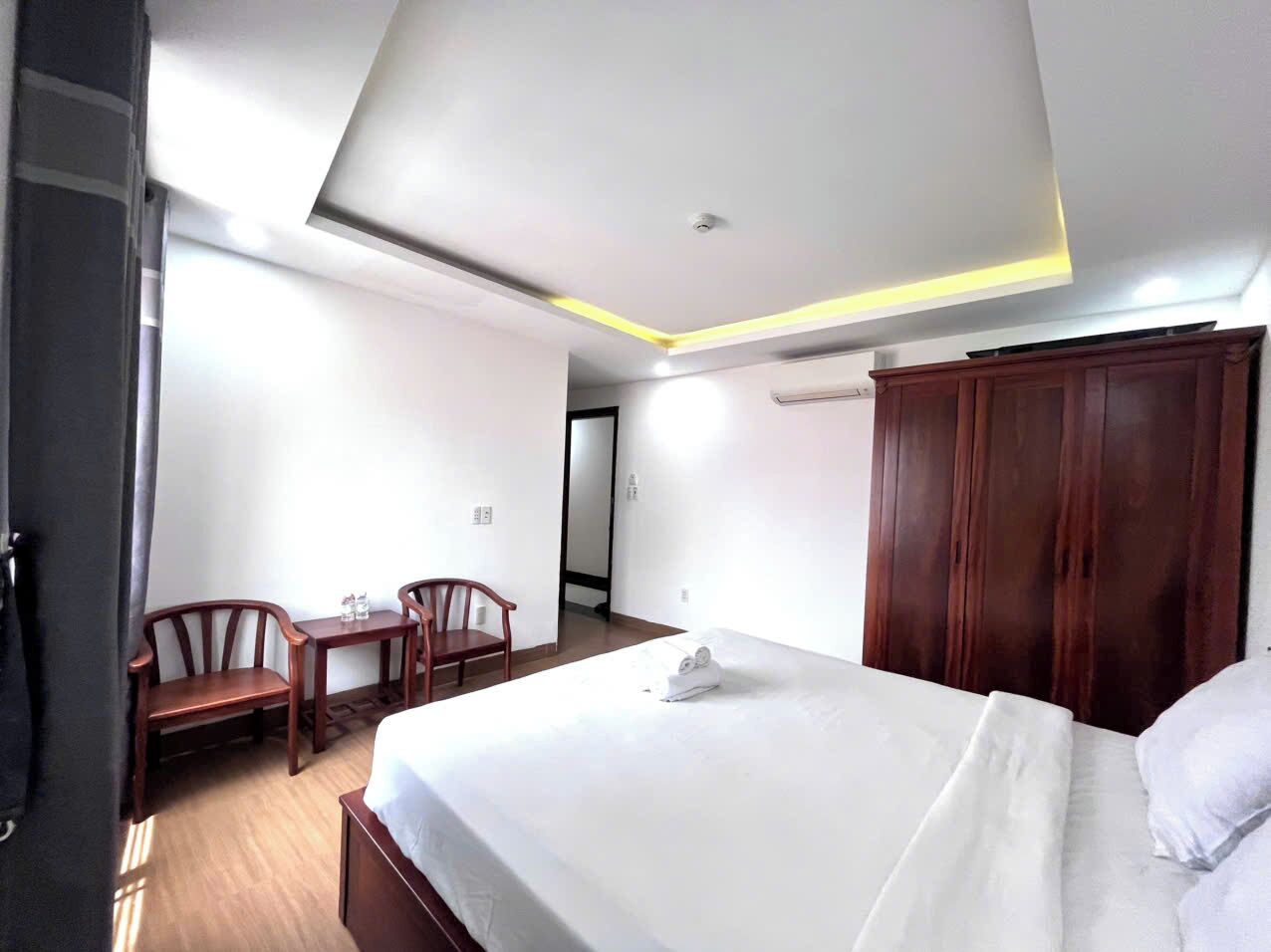 Une chambre d’hôtel comprenant un lit, un bureau, deux chaises, une armoire et une porte donnant sur une autre pièce.