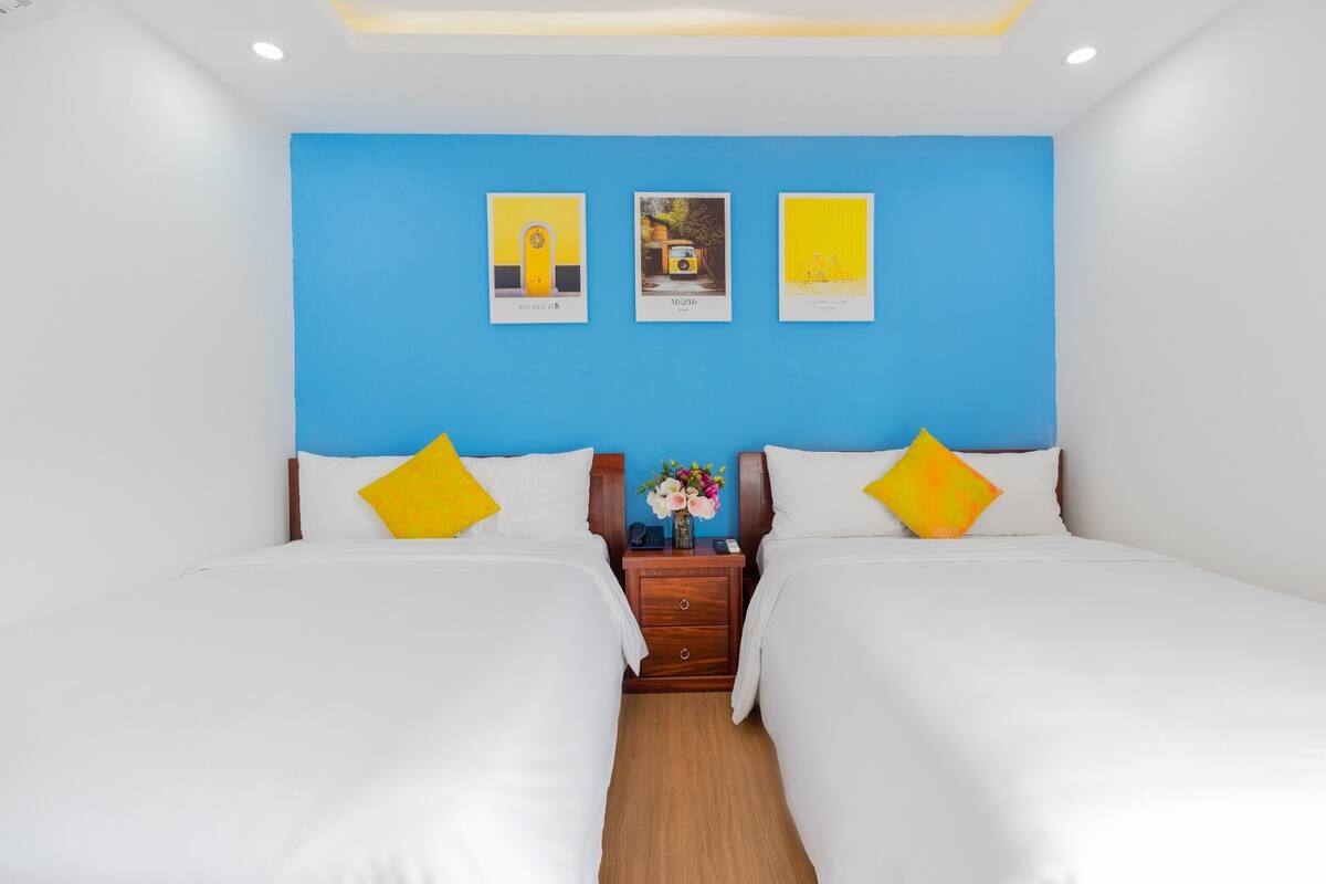 A hotel room with two beds, a wooden nightstand, and three framed pictures on the wall.