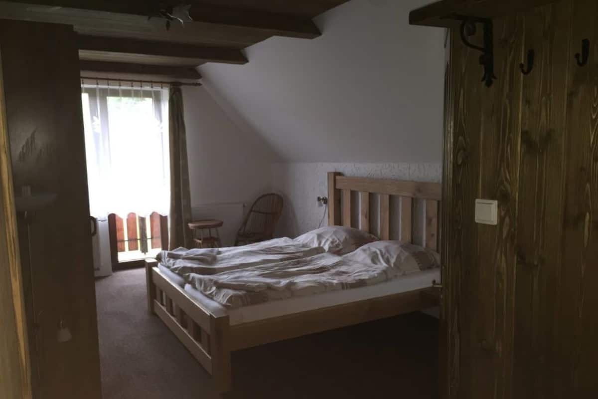A bedroom with a wooden bed, a chair, and a window with curtains.