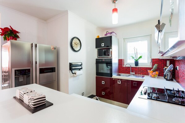 A modern kitchen with stainless steel appliances, a red tiled backsplash, and a window providing natural light.