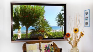 Habitación con una ventana grande que ofrece vistas a la costa, un sofá de mimbre, una mesita con un florero y un jarrón decorativo con girasoles.