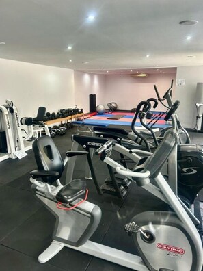 A gym with cardio machines, weightlifting equipment, and a blue mat area. - Nura Condor (Palma de Mallorca)