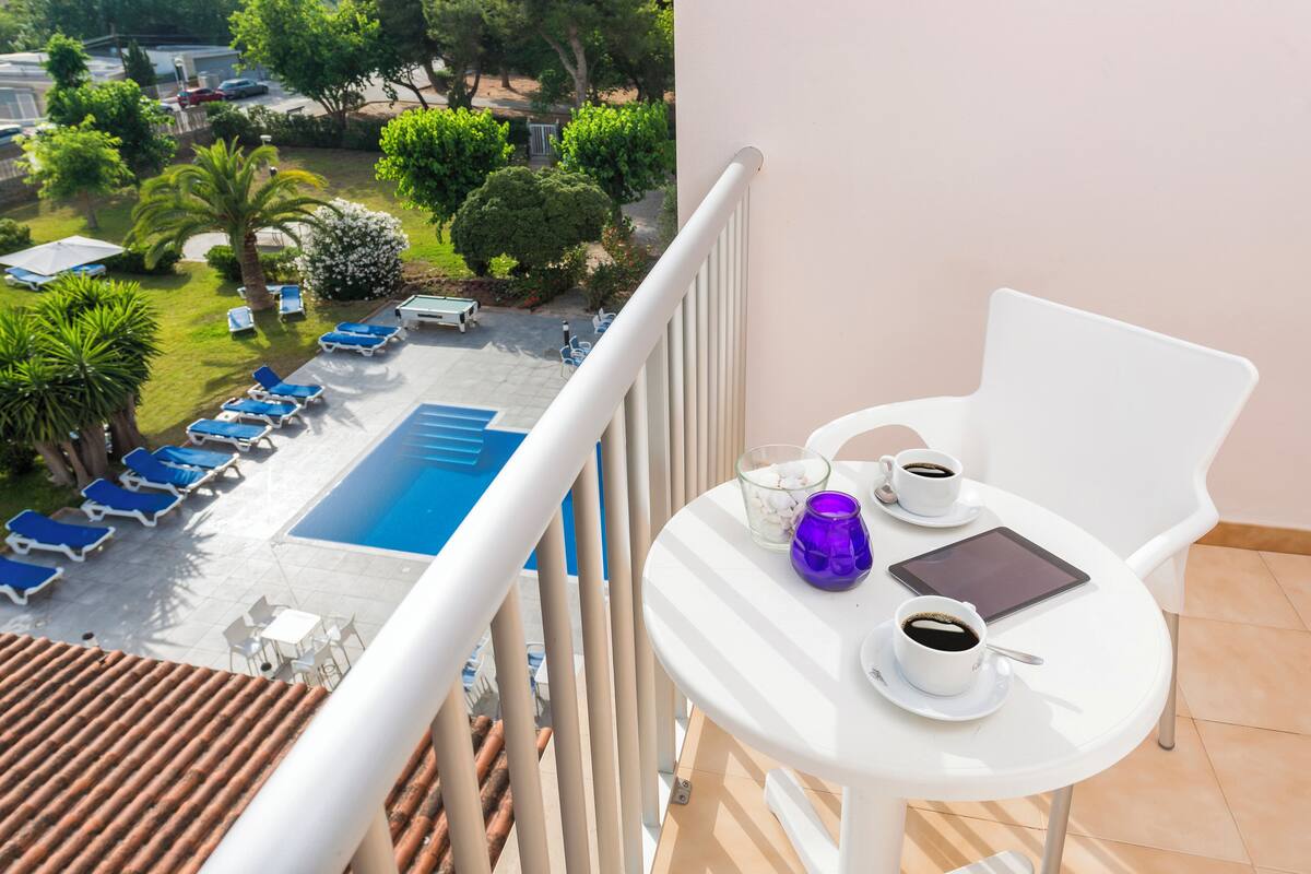 A balcony with a pool view, a table with cups and a tablet, and lounge chairs.