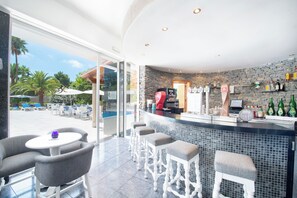 Zona de bar con pared de piedra, asientos y vista a la piscina exterior.
