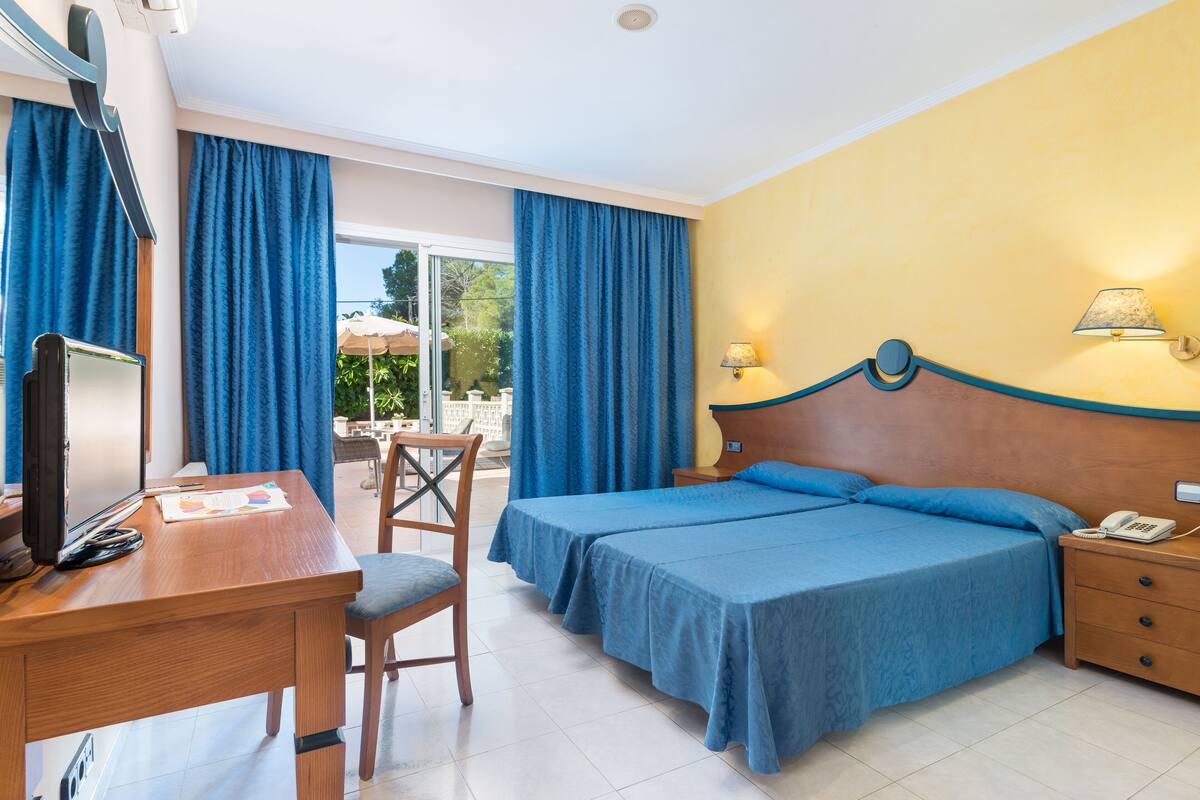A hotel room with a bed, a desk, a chair, a TV, and a phone on the nightstand.