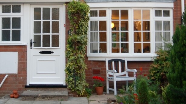 Una casa de dos pisos con fachada blanca, una puerta principal y una ventana con marco blanco.